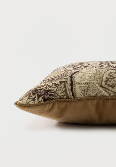 Coussin décoratif avec motif floral et géométrique marron et beige sur le dessus et tissu uni marron sur le bord inférieur.