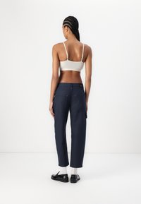 Marineblauwe cargo-broeken met zijzakken, gestyled met een crèmekleurige bralette. Soepele stof, losse pasvorm en details met contrasterende stiksels.