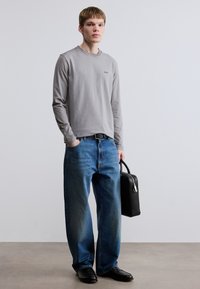 Γκρι πουκάμισο μακρυμάνικο με μικρό λογότυπο, μπλε τζιν φαρδιάς γραμμής, μαύρα παπούτσια και μαύρη τσάντα. Απλός σχεδιασμός με ελάχιστες λεπτομέρειες.