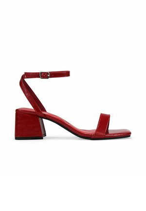 Sandal de tacón cuadrado de cuero rojo, con puntera cuadrada, tira en el tobillo y acabado suave. Presenta un diseño minimalista con un aspecto brillante.