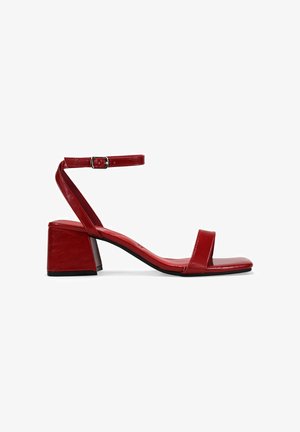 Sandal de tacón cuadrado de cuero rojo, con puntera cuadrada, tira en el tobillo y acabado suave. Presenta un diseño minimalista con un aspecto brillante.