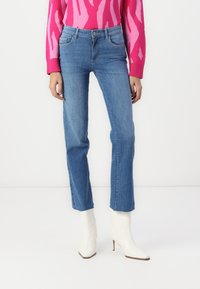 Jeans de mezclilla azul de pierna recta con cinco bolsillos y costuras sutiles, combinados con botas de tobillo blancas con punta y un suéter de diseño rosa.