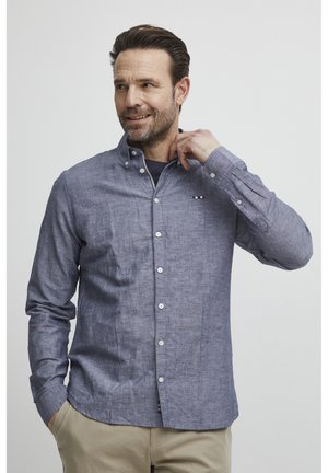 Menns knapp-up skjorte i blå chambray-stoff, med en klassisk krage, frontknapper og en liten flerfarget logo på brystet.