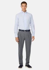 Camicia a righe blu chiaro e bianca, maniche lunghe, colletto botton-down, abbinata a pantaloni grigi plissè, cintura intrecciata blu scuro, scarpe blu navy.