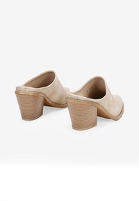 Mulos de cuero beige con punta redonda y un tacón apilado texturizado. El interior es suave y cuenta con una plantilla acolchada.