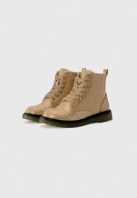 Une paire de bottines à lacets brillantes dorées avec des semelles noires sur un fond clair.