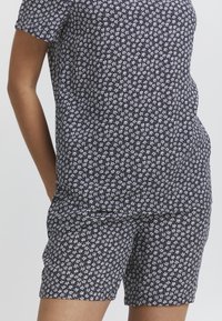 Set di maglietta a maniche corte e pantaloni corti con motivo floreale nero. Il tessuto è leggero e presenta piccoli fiori bianchi sparsi. Design semplice e dal taglio rilassato.