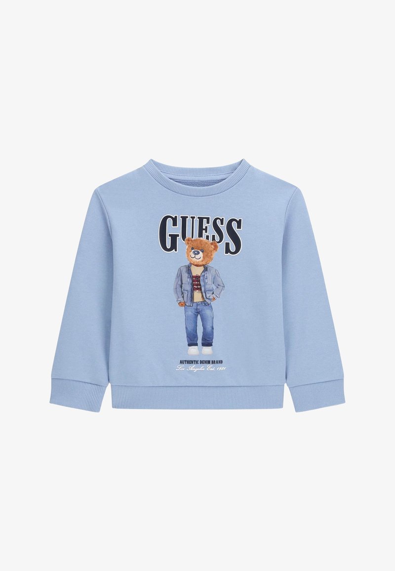 Világoskék pulóver, melyen egy farmerdzsekit és farmert viselő medve látható, a "GUESS" felirattal fölötte, és az "Authentic Denim Brand" felirattal alatta.