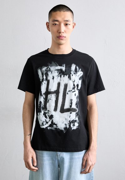 T-shirt en coton noir avec un graphisme audacieux imprimé en blanc représentant les lettres "HL" et des coups de pinceau abstraits en noir. Col rond et manches courtes.