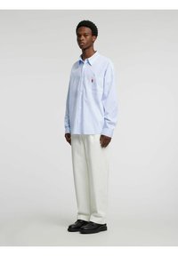 Modra in bela črtasta srajca z gumbi, dolgimi rokavi in prsnim žepom z majhnim vezenim vzorcem, kombinirana z belimi hlačami.