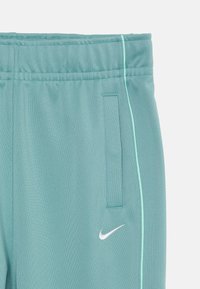 Pantalons de sport turquoise clair en tissu doux, dotés d'une taille élastique, de garnitures décoratives sur les côtés et d'un logo Nike blanc.