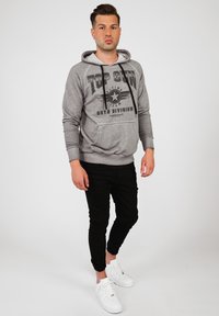 Grå hoodie med svart "TOP GUN" grafik och stjärndetalj. Svarta avsmalnande byxor, vita sneakers. Slät textur och avslappnad design.