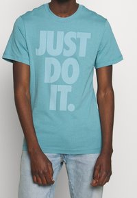 Tykevně modré bavlněné tričko s kulatým výstřihem a krátkými rukávy. Na přední straně se nachází nápis "JUST DO IT." ve velkých, světlých písmenech.