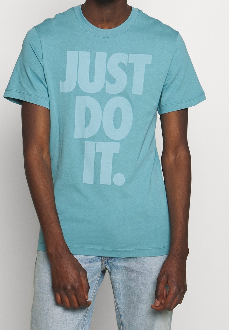 Tykevně modré bavlněné tričko s kulatým výstřihem a krátkými rukávy. Na přední straně se nachází nápis "JUST DO IT." ve velkých, světlých písmenech.