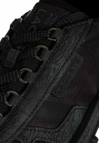 Sneaker nera in pelle testurizzata con una leggera lucentezza, dettagli in mesh e accessori metallici. Logo embossato sul lato e sui lacci.