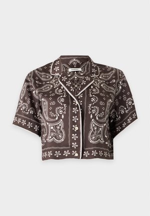 Femme portant une chemise boutonnée à manches courtes à motif cachemire foncé et une jupe à volants asymétrique assortie avec des sandales à talons noires.