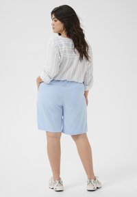 Ljusblå shorts i slätt tyg, med en bakficka. I kombination med en långärmad skjorta med ljusa ränder. Avslappnade skor.