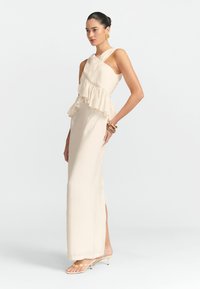 Robe couleur crème avec une taille à peplum froncé, décolleté asymétrique et silhouette ajustée. Portez-la avec des sandales à talons transparents.