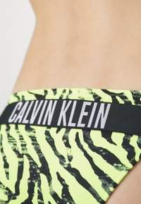 Bikini kalhotky Calvin Klein s černým a neonově žlutým vzorem tygřích proužků, s kontrastním černým elastickým pasem a logem.