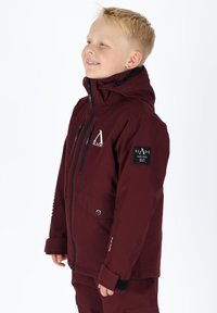 Giacca da neve bordeaux con cappuccio, dotata di tasche con zip, toppe con logo e un tessuto testurizzato per calore e durata.