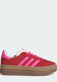 Baskets en daim rouge avec des accents roses, trois bandes roses, lacets blancs et talon blanc texturé. Semelle plateforme en caoutchouc marron.