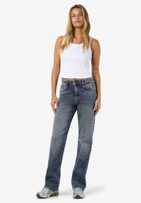 Svetlomodré rovné rifle z denimu so stredne vysokým pásom, s návrhom piatich vreciek a jemným vyblednutím; skombinované s bielym tielkom bez rukávov.