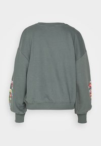 Pull vert oversized avec un col rond et des manches bouffantes. Présente des broderies florales colorées sur les deux manches. Texture douce.
