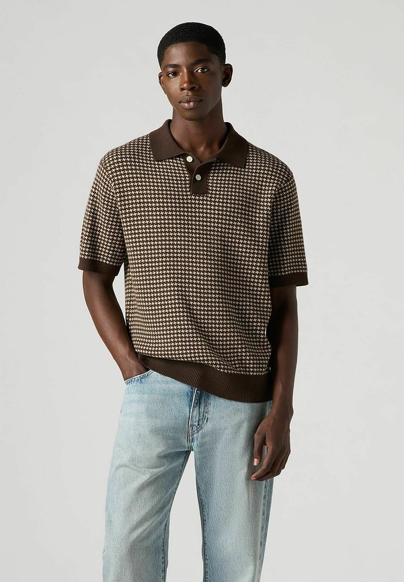 Ruskea houndstooth-kuosisella polo-paidalla, tummalla kauluksella ja resoripäällä, yhdistettynä vaaleansinisiin farkkusaumoihin.