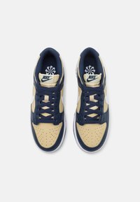 Sneakers Nike con tomaia in pelle beige con dettagli blu navy, punta perforata, swoosh bianco e lacci blu scuro.
