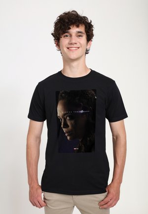 Sort T-shirt med et grafisk print af en kvindelig karakters profil på en mørk baggrund, som fremhæver detaljerede ansigtstræk og udtryk.