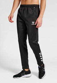 Zwarte sportieve broek met een elastische tailleband, voorzien van een wit logo en zijstrepen. Soepele stof, taps toelopende pasvorm en enkel-lang ontwerp.