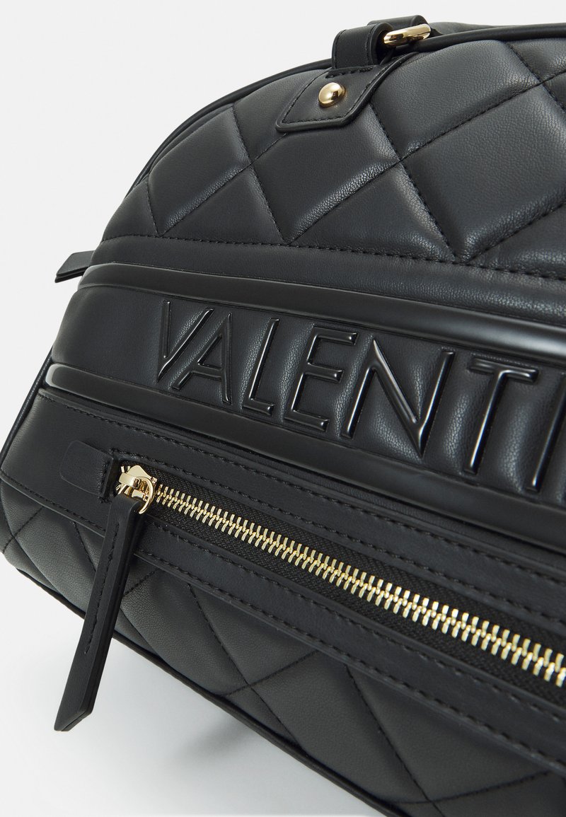 Schwarze, gesteppte Lederhandtasche mit goldfarbenem Reißverschluss, geprägt mit dem Logo "VALENTIN" und einem kleinen schwarzen Reißverschlussanhänger. Texturierte Oberfläche mit glatten Akzenten.