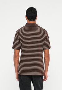 Man wearing a brown short-sleeve polo shirt with white horizontal stripes, shown from the back against a plain white background.