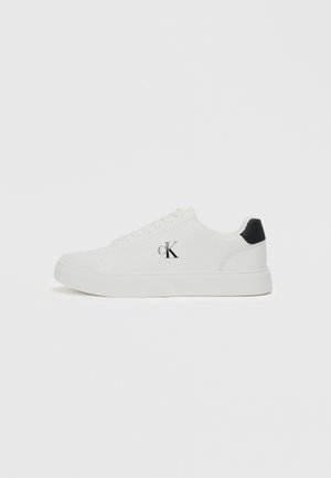 White sneaker with smooth leather upper, round toe, black heel accent, and "CK" logo on the side. Features a lace-up design and flat sole.