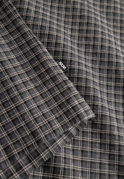 Tekstilna tkanina u tamnosivoj boji s bijelim mrežastim uzorkom. Mekana tekstura, tkan dizajn, prikazuje zavoj u kutu i malu oznaku brenda.