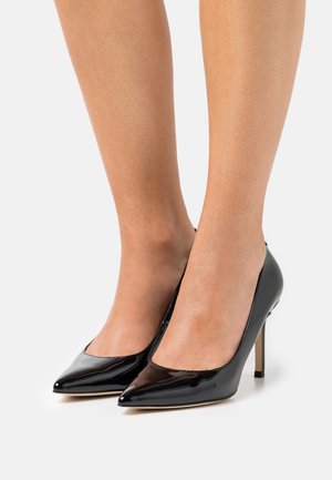 Decolleté nere in vernice con punta affilata e tacco a stiletto sottile. La superficie è lucida, con una texture liscia.