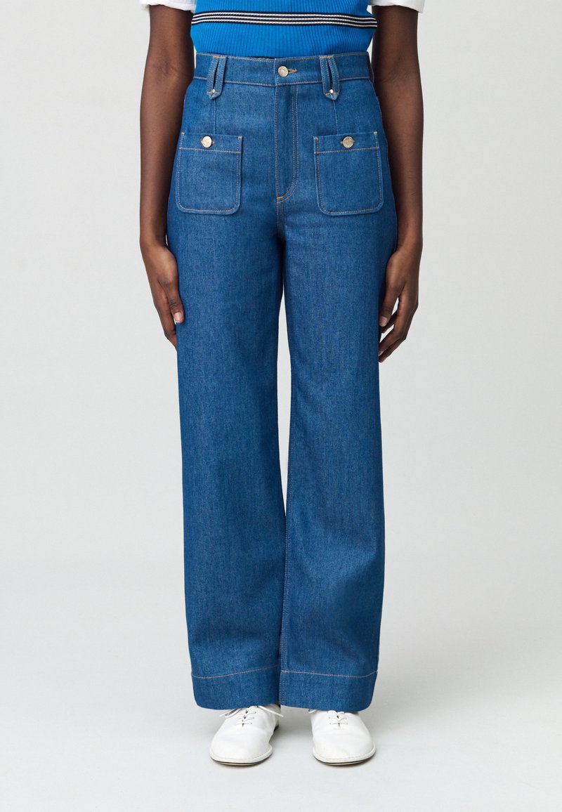 Pantalons en denim bleu taille haute, à jambe large, avec poches avant et finitions soignées. Présentent une texture lisse et des détails de couture contrastants.