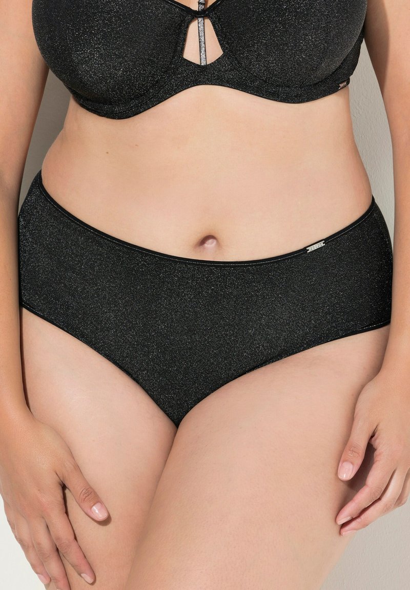 Zwarte, hooggeknipte onderbroek met een subtiele glans. Gladde textuur, eenvoudige uitstraling, met een klein metalen logoaccent op de tailleband.