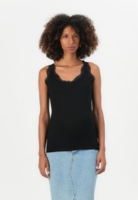 Svart topp med bølget blondekant. Tettsittende design laget av mykt, elastisk materiale. Brukt sammen med en lys blå denimskjørt.
