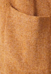 Suéter de punto en un cálido tono naranja con un acabado texturizado. Cuenta con un bolsillo frontal y una tela suave y lisa.