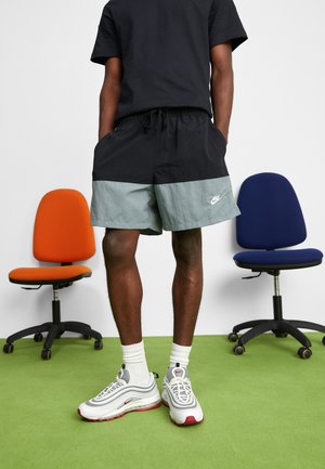 Pantaloni corti neri e grigi chiari con vita elastica, con logo Nike bianco. Abbinati a scarpe Nike grigie e rosse e calze bianche.