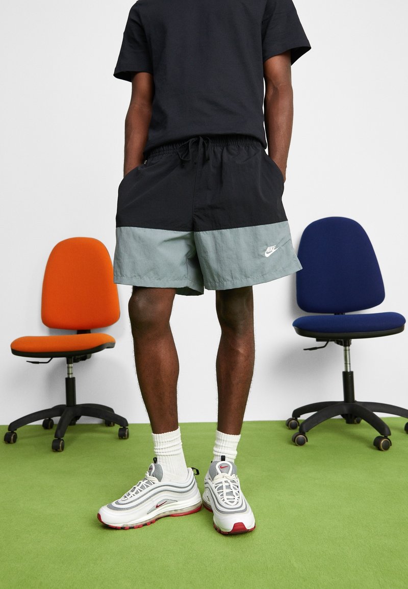 Černé a světle šedé kraťasy s elastickým pasem, s bílým logem Nike. V kombinaci se šedými a červenými botami Nike a bílými ponožkami.