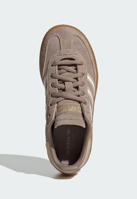 Baskets en daim marron avec des rayures blanches, des lacets texturés et des accents dorés. Bout arrondi et semelle en caoutchouc de couleur gomme.