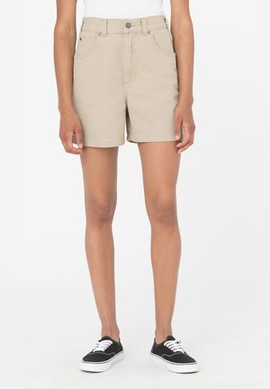 Beige denim shorts med høj talje, forlommer og oprevne kanter, parret med sorte lærredssneakers.