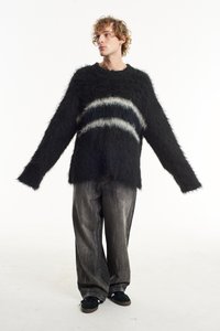 Black fluffy sweater with wide sleeves and a horizontal white and grey striped pattern, paired with loose grey jeans and black shoes.