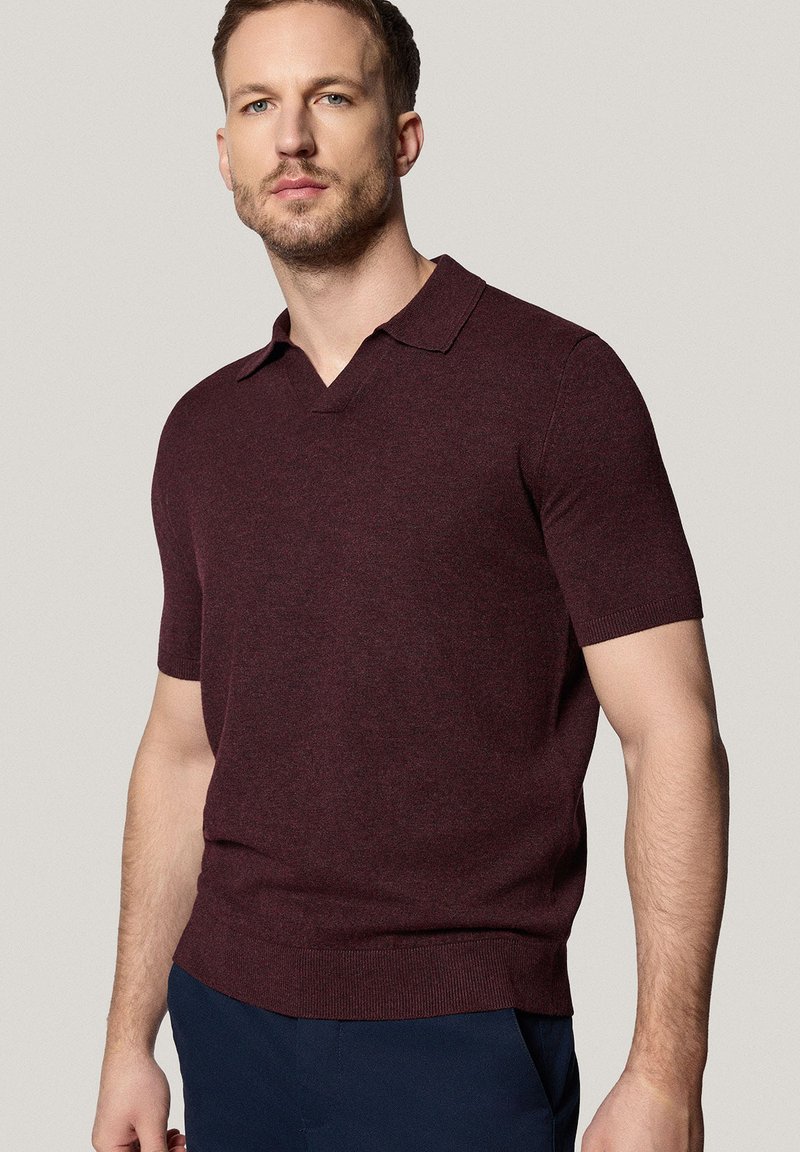 Koszulka polo z krótkim rękawem w ciemnym burgundzie, wykonana z fakturowanej tkaniny. Posiada kołnierzyk w kształcie litery V oraz ribbowany dół. Prosty fason.