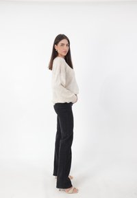 Jasno beżowy, oversize'owy sweter o fakturowanym wykończeniu, zestawiony z czarnymi, wysokiej talii dzwonami i beżowymi sandałami na obcasie.