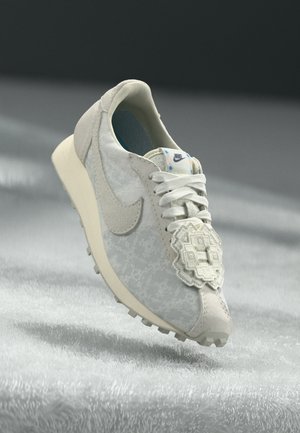 Chaussure de sport blanche avec une tige texturée, un système de laçage, un logo bien en vue et une semelle lisse avec de petites pointes de traction.