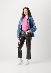 Džínová bunda, růžová košile s krátkým rukávem, lesklé čern�é vinylové kalhoty, bílé tenisky. Na kalhotách je viditelný přívěsek na klíče.