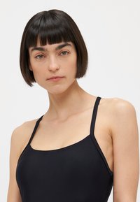 Zwarte, aansluitende badkleding met dunne bandjes. Eenvoudig ontwerp met een vierkante halslijn en een gladde textuur. Geschikt voor wateractiviteiten.